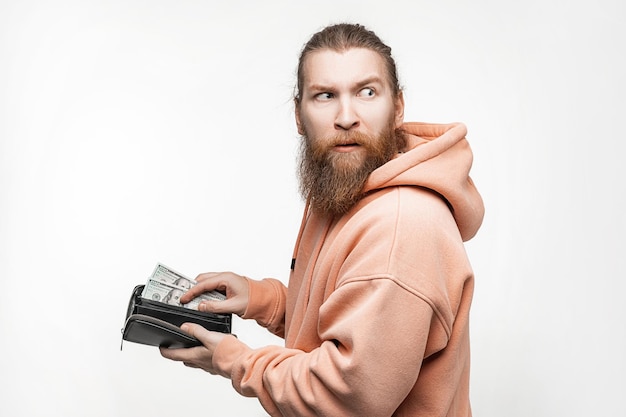 Handsom man holding paper currency in wallet and is unhappy on gray background Hand pulling 100 dollars banknotes from wallet Guy have cash The concept of money salary finance investment save