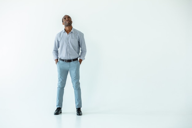 Handsome adult afro american man being involved in toughts while standing isolated on white wall