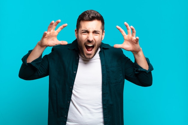 Handsome adult blond man screaming in panic or anger, shocked, terrified or furious, with hands next to head