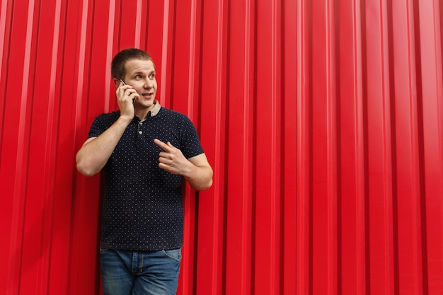 Handsome adult man using his cellphone, talking on red wall