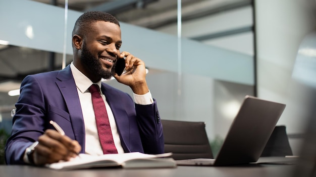 Handsome african american businessman working on laptop having phone conversation