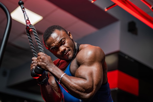 Handsome african american fitness trainer doing workout for hands in gym Modern equipment for sport View from below