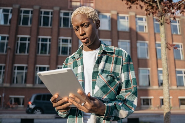 handsome African American man holding digital tablet reading ebook walking on the street