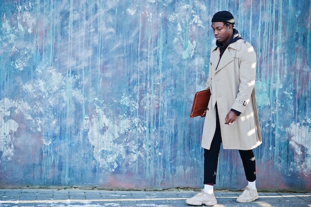 Handsome african american man posing outside in black hat and beige coat with folder in hand