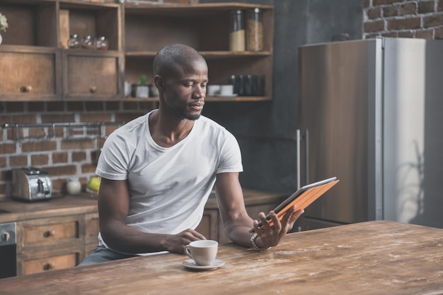 Handsome african american man using tablet while having his morning coffee at home