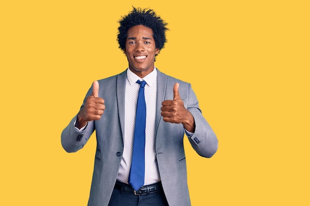 Handsome african american man with afro hair wearing business jacket success sign doing positive gesture with hand thumbs up smiling and happy cheerful expression and winner gesture