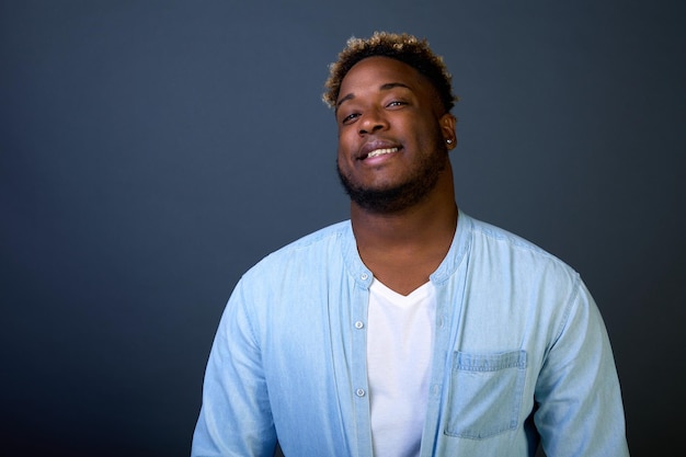 Handsome AfricanAmerican man in a blue shirt smiles against a black background