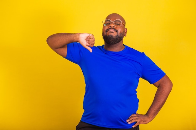 Handsome afro brazilian man wearing glasses blue shirt over yellow background thumbs down disapproving disappointment disappointed disapproving negative