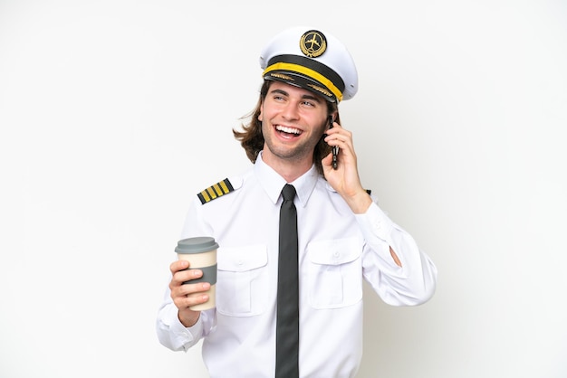 Handsome Airplane pilot isolated on white background holding coffee to take away and a mobile