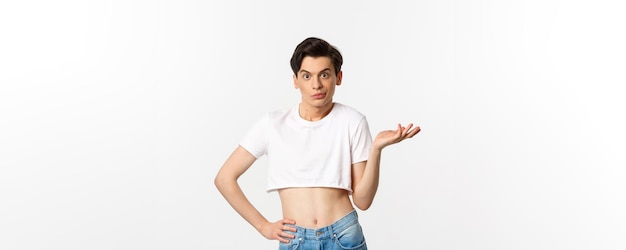 Handsome androgynous man in crop top looking confused shrugging clueless standing over white background