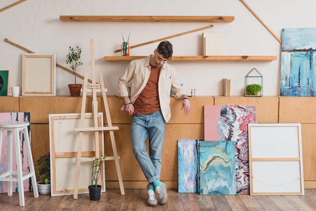 Handsome artist in pink shirt and blue jeans standing in spacious gallery