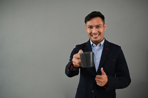 Handsome Asian businessman holding a coffee cup standing on an isolated grey background