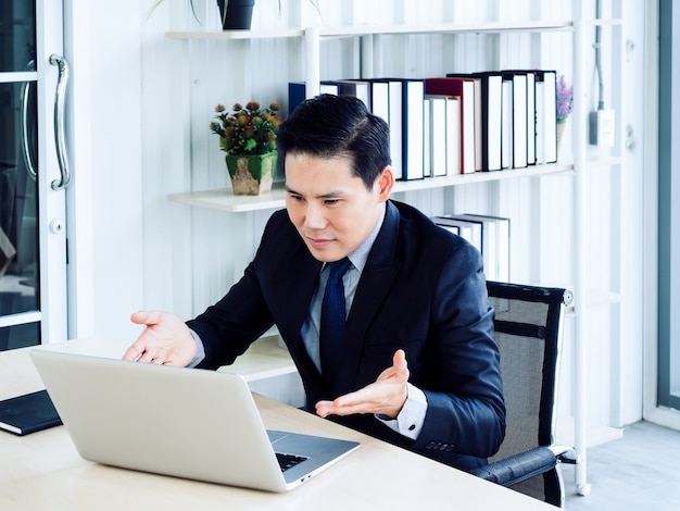 Handsome Asian businessman in suit video call, explaining to colleague through laptop computer in meeting online working, video conference