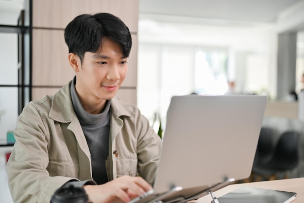 Handsome Asian male office worker or developer working on his task on laptop in the office