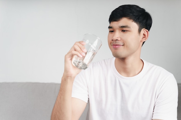 Handsome asian man drinking a glass of water on the sofa at living room