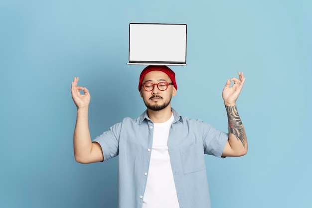 handsome asian man freelancer holding laptop computer on head practicing yoga isolated