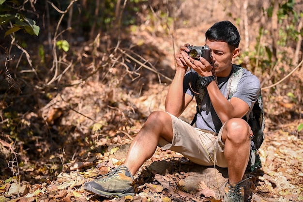 Handsome Asian man taking a picture with film camera while hiking at the mountain trail