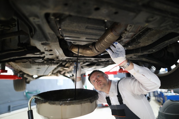 Handsome auto mechanic checks undercarriage of car at service station