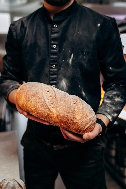 Handsome baker in uniform holding freshly baked bread at the bakery