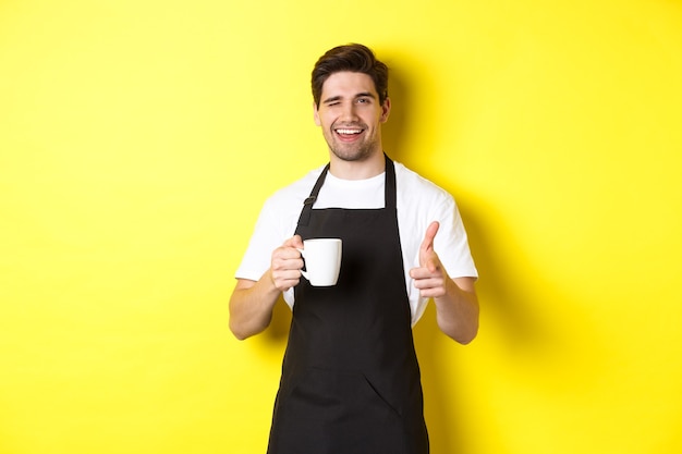 Handsome barista in black apron holding coffee cup