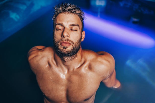 Handsome beard man floating in tank filled with dense salt water used in meditation, therapy, and alternative medicine.