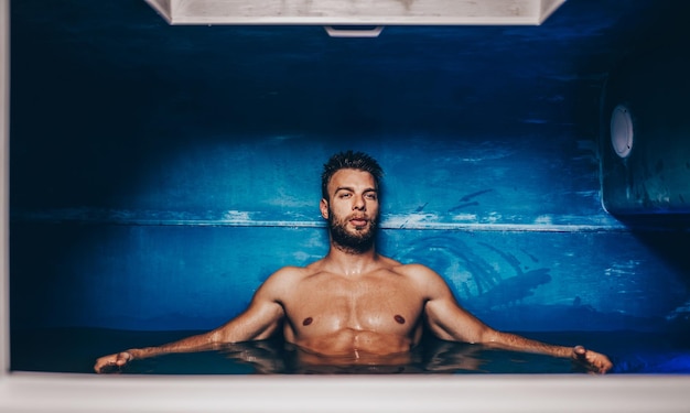 Handsome beard man floating in tank filled with dense salt water used in meditation, therapy, and alternative medicine.