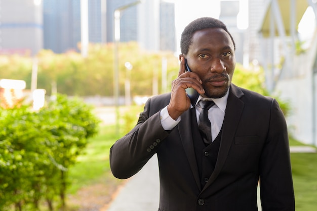 Handsome bearded African businessman talking on the phone at the park