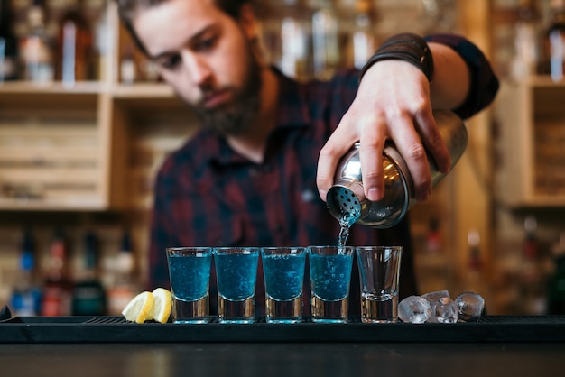 Handsome bearded barman is making cocktails in night club.