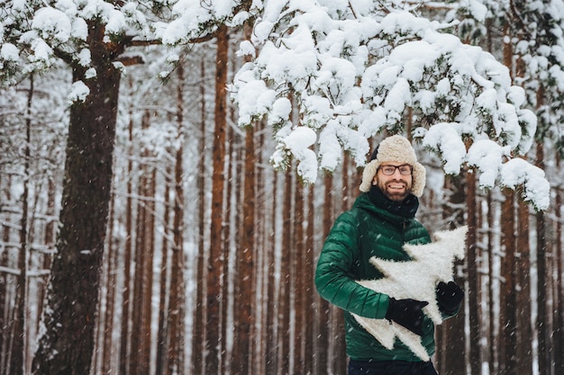 Handsome bearded male wears warm fur cap with ear flaps and green anorak