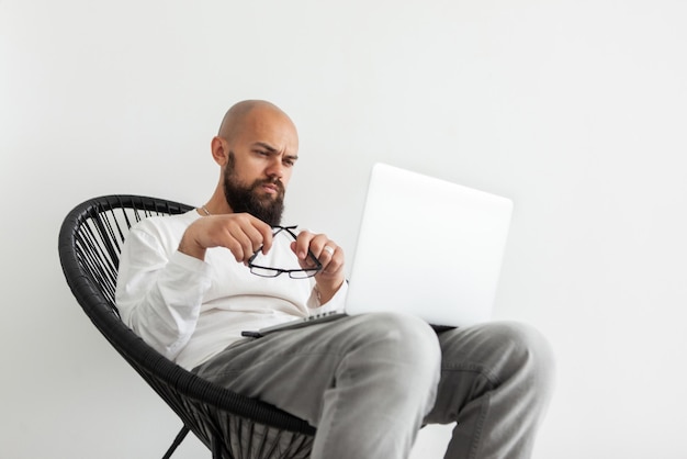 Handsome bearded man freelancer looks attentively into laptop screen while sitting in armchair on white background