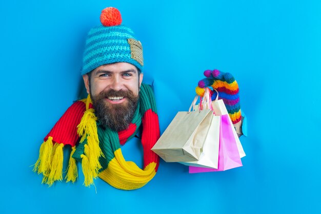 Handsome bearded man holds shops packet in hand through a paper hole bearded man in warm colourful