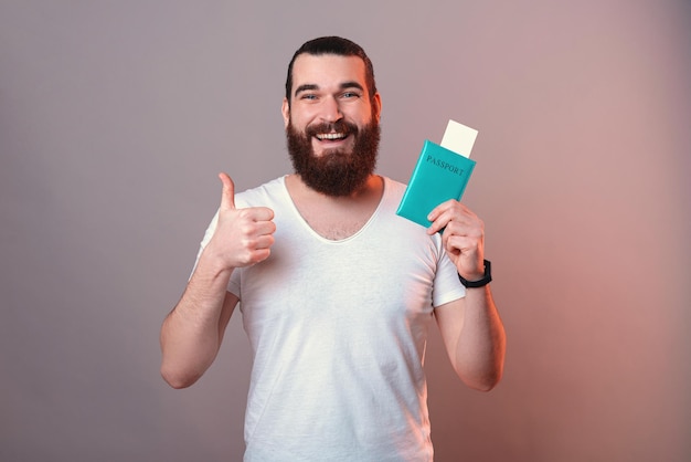 Handsome bearded man is showing thumb up while holding a passport