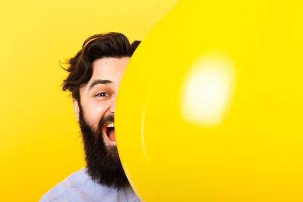 Handsome bearded man smiling from above yellow balloon on yellow background, positive emotions