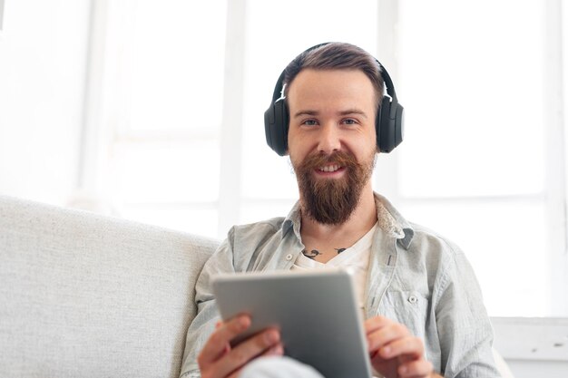 Handsome bearded man using digital tablet while resting on couch at home