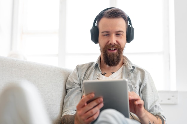 Handsome bearded man using digital tablet while resting on couch at home