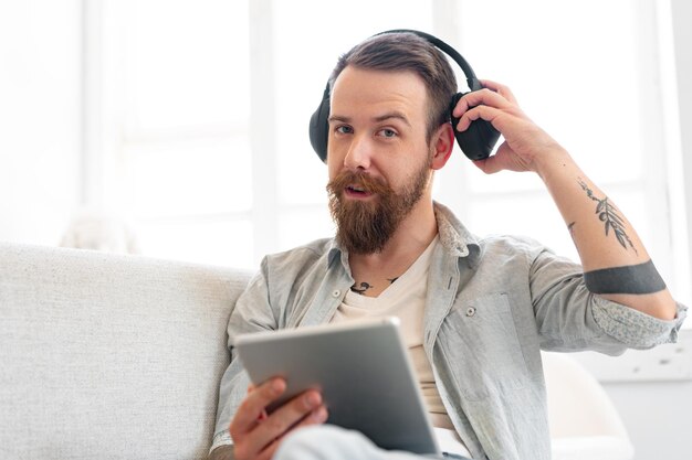 Handsome bearded man using digital tablet while resting on couch at home