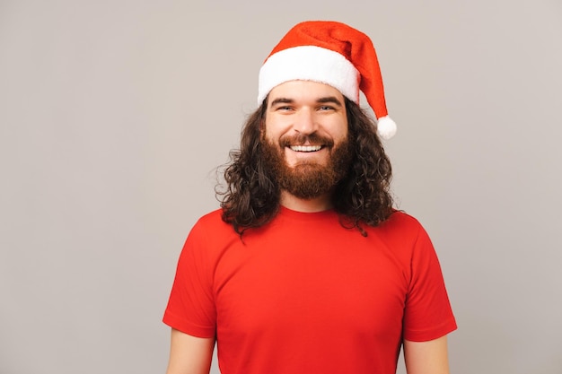 Handsome bearded man wearing red Christmas cap is smiling at the camera