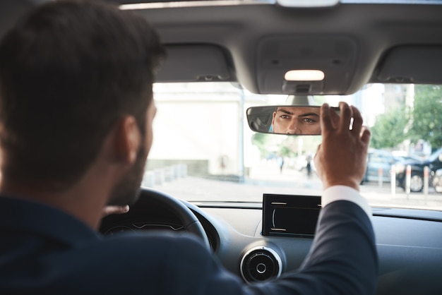 Handsome bisnessman behind the wheel adjusting rear view mirror