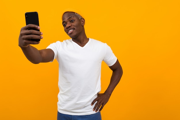 Handsome black african man makes selfie on the phone on orange with copy space