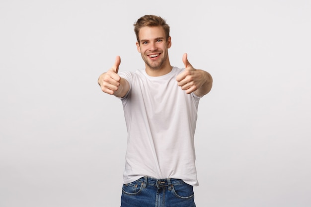 Handsome blond guy with blue eyes and white T-shirt giving thumbs up