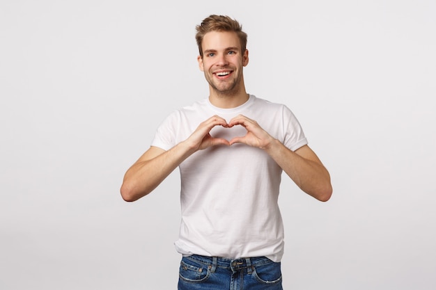 Handsome blond guy with blue eyes and white T-shirt showing heart sign