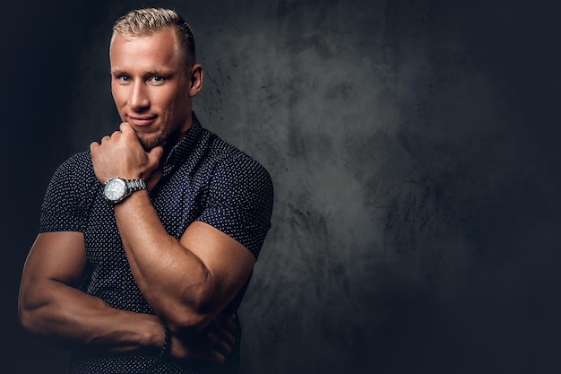 Handsome blond man in a dark blue shirt posing over grey background in a studio.