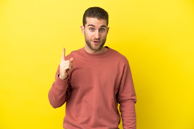 Handsome blonde man over isolated yellow background intending to realizes the solution while lifting a finger up