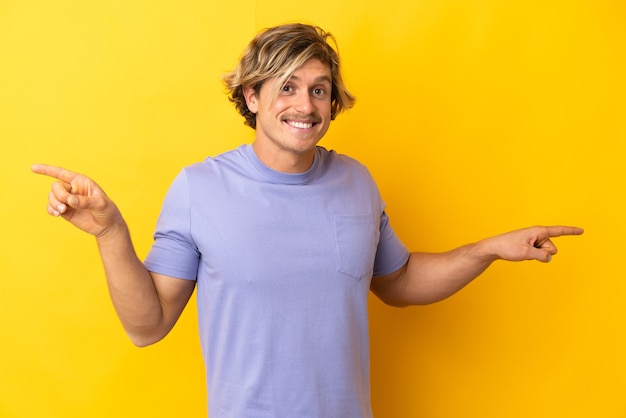 Handsome blonde man isolated on yellow wall pointing finger to the laterals and happy