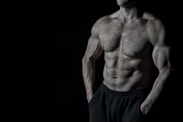 Handsome bodybuilder man or sexy muscular guy with athlete body, torso and chest training sport and posing in gym on black background, copy space