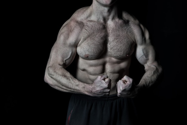 Handsome bodybuilder man or sexy muscular guy with athlete body, torso and chest training sport and posing in gym on black background, copy space