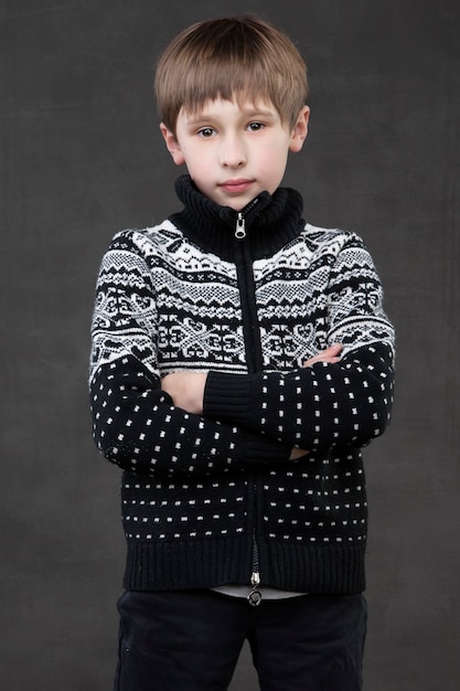 Handsome boy in a knitted jacket on a gray background. Pensive child. School-age boy.