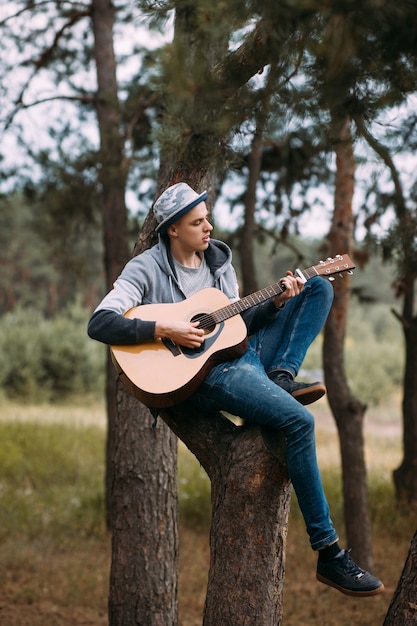 Handsome boy playing guitar tree forest concept. Unity with nature. Hiking happy moments.