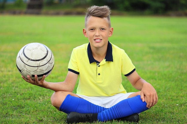 Photo handsome boy soccer player sitting on the soccer field