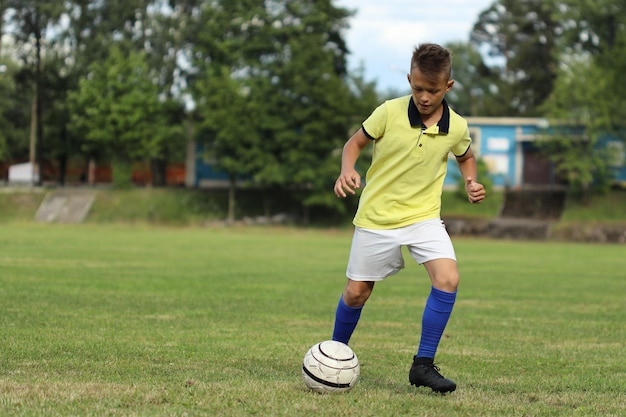 Handsome boy soccer player in a yellow t-shirt on the soccer field plays with a ball